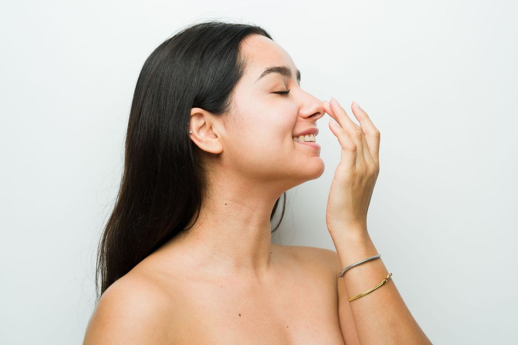 Woman smiling while applying skincare to her face against a white background