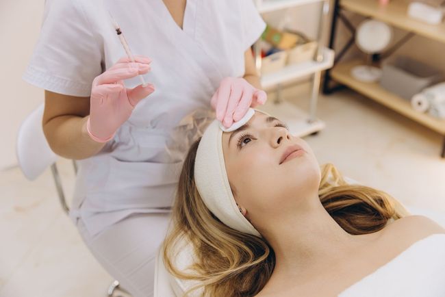 Cosmetician applying a facial treatment to a reclining client in a spa room