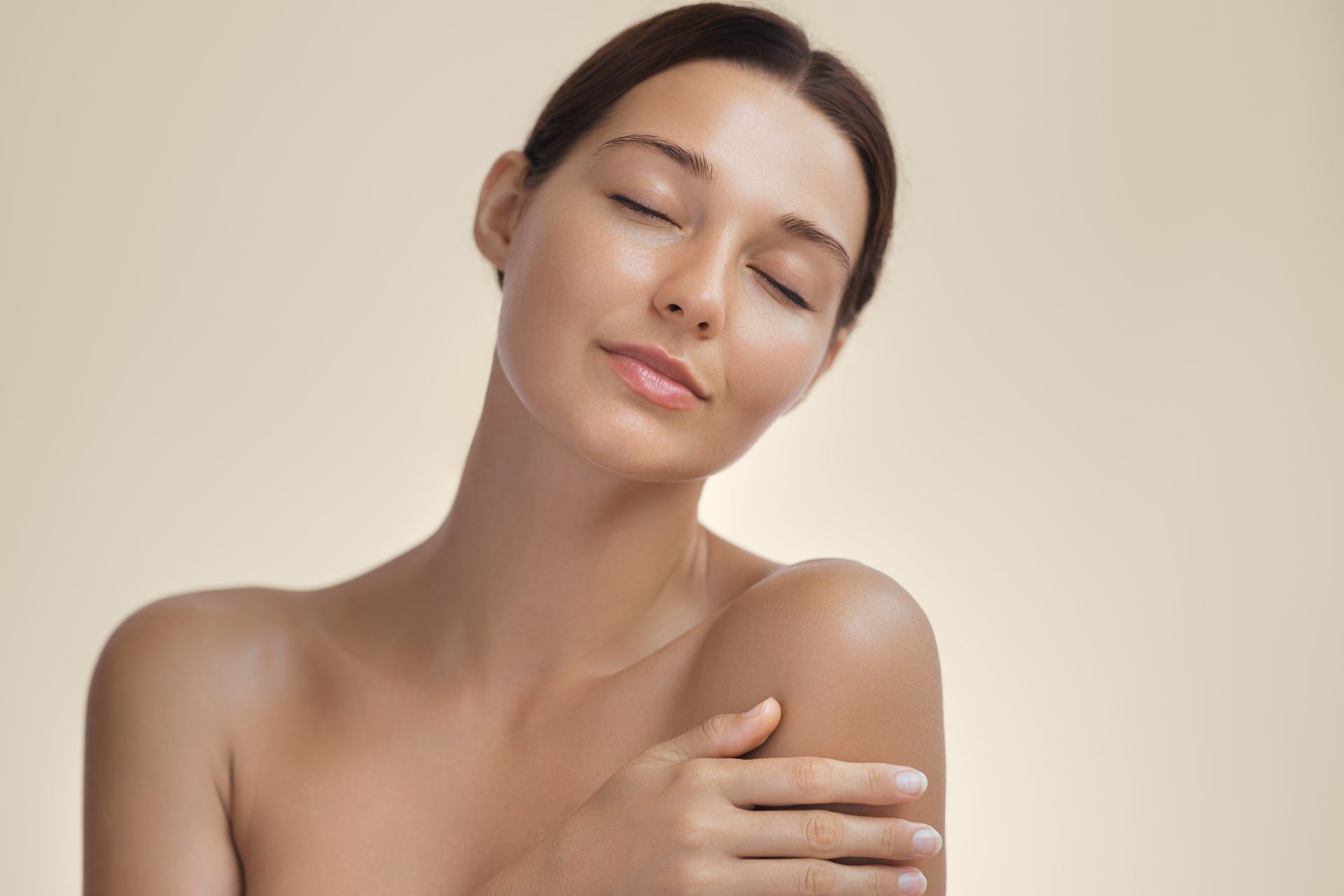 Woman with closed eyes gently touching her shoulder against a beige background