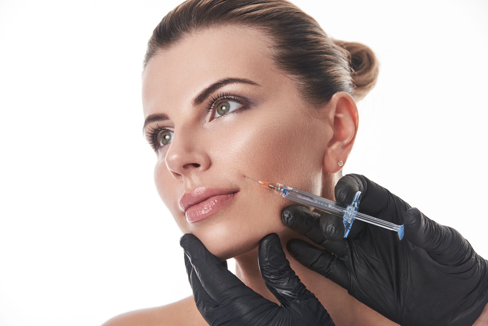 Gloved hands injecting a woman’s cheek with a cosmetic syringe