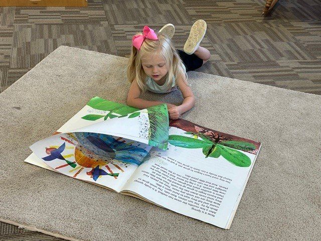 A little girl is laying on the floor reading a book