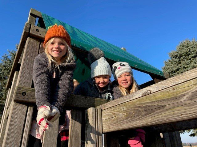 Three little girls are playing on a wooden playground.