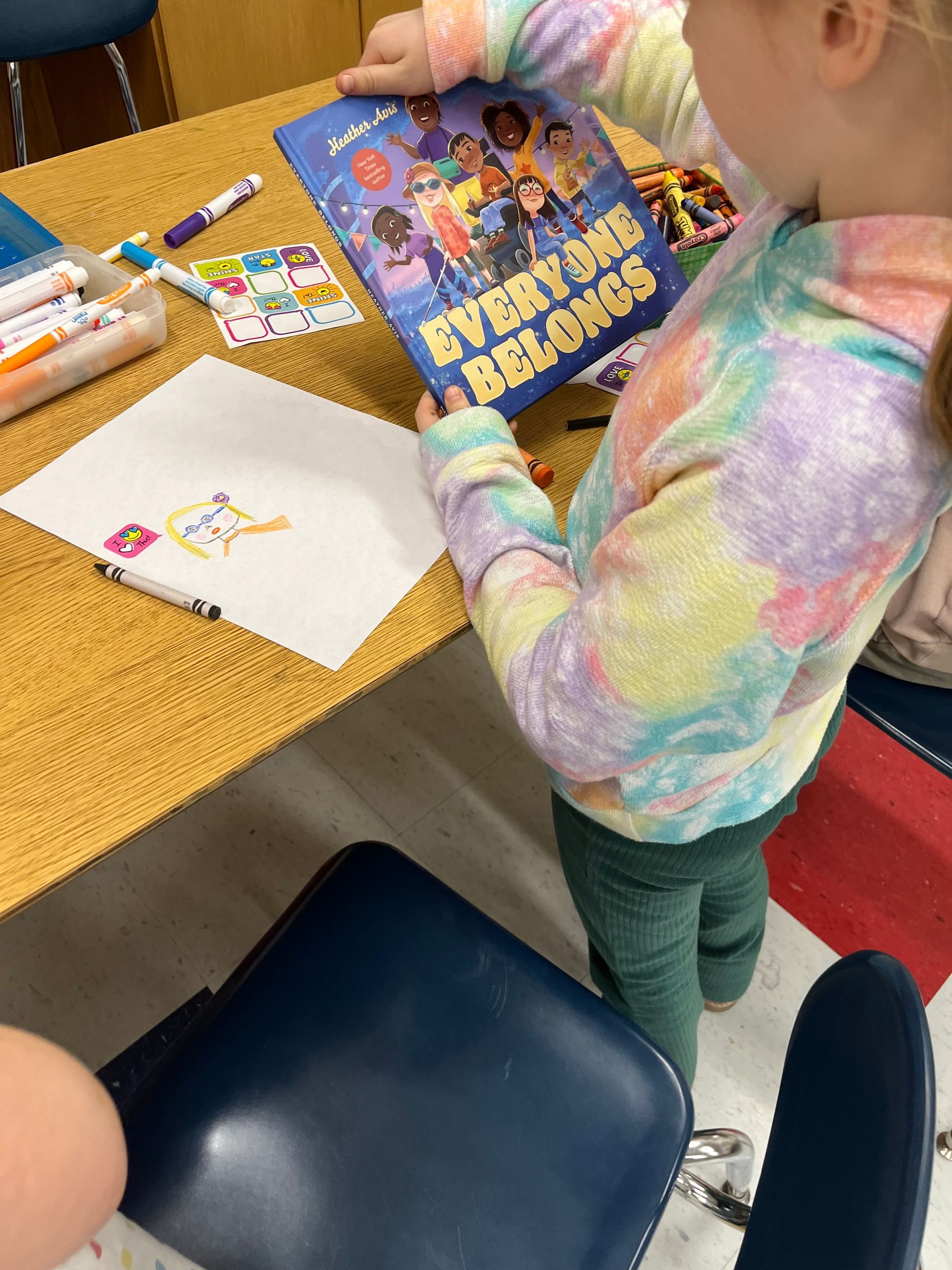 A little girl is holding a book titled everyone belongs.