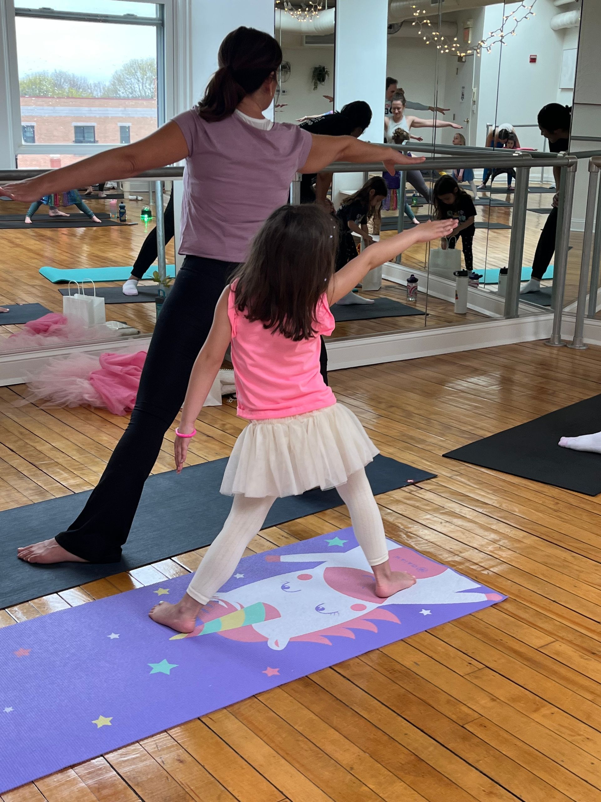 A woman and a little girl are practicing yoga in a gym.