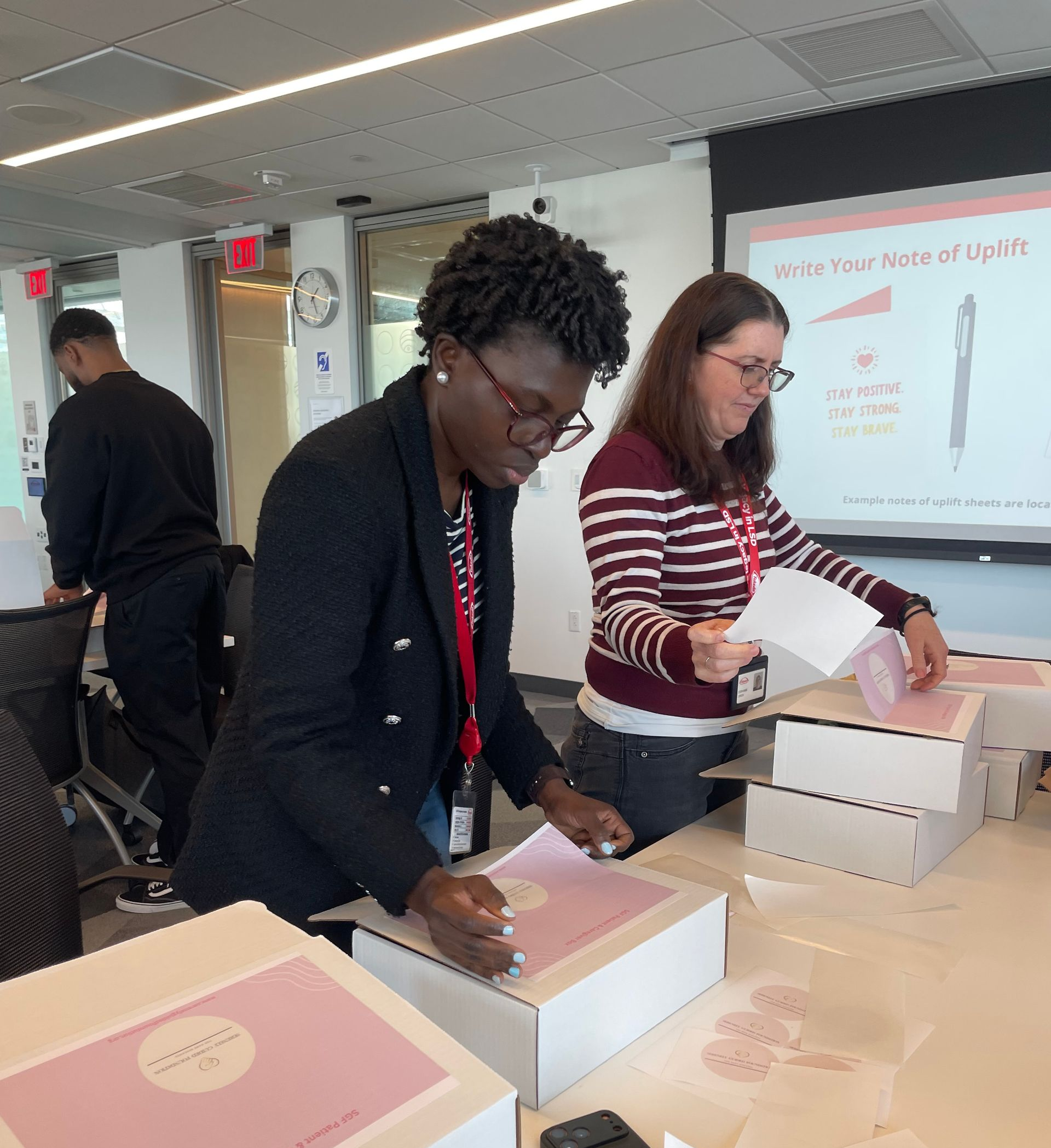 People packing boxes at a table in a classroom or workshop setting with a presentation screen in the background