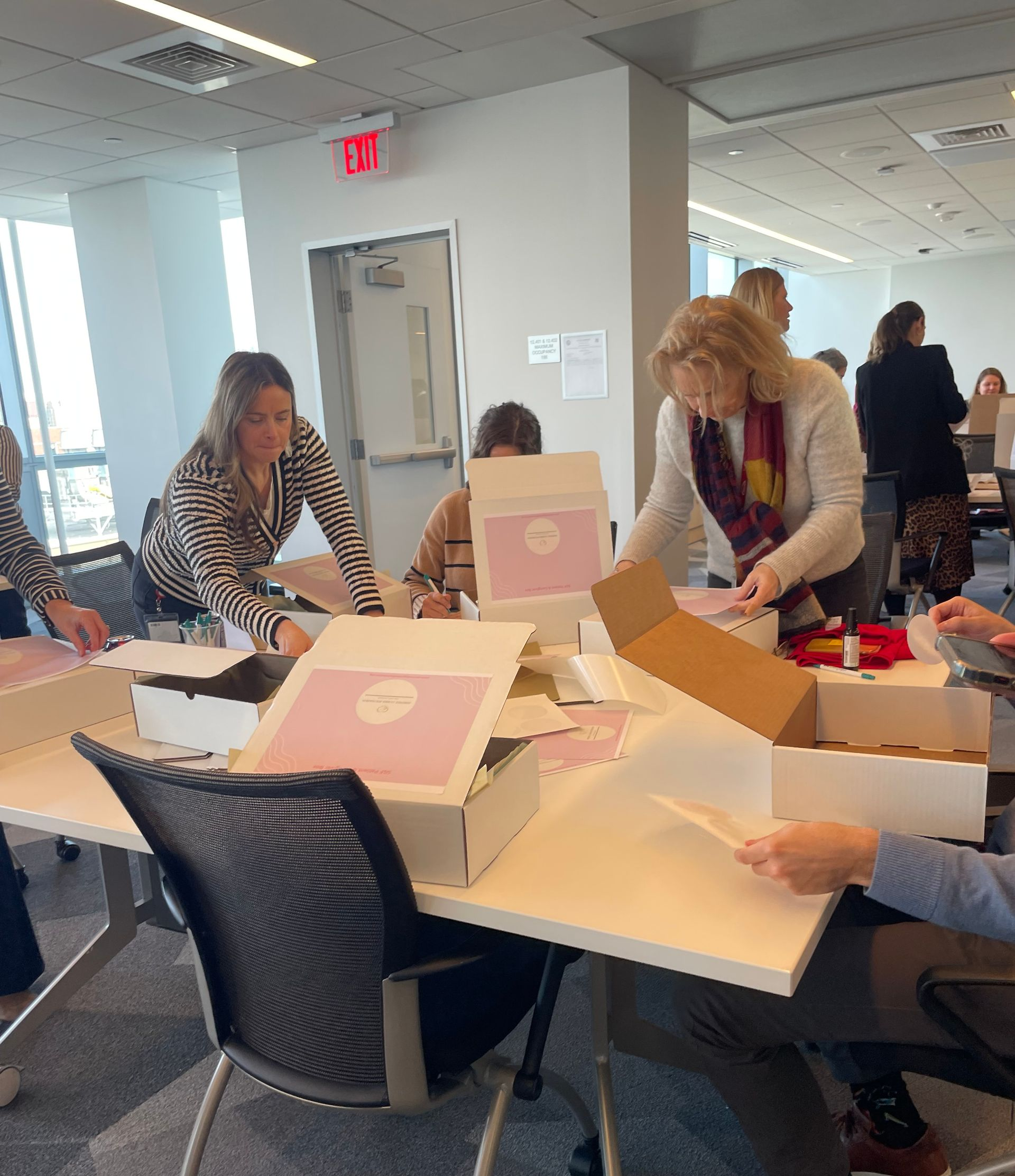 People packing boxes around a table in a bright office or meeting room