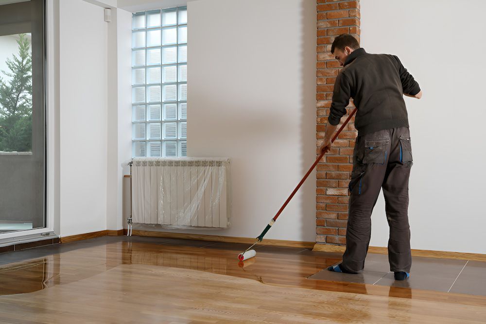 A Man Is Painting A Wooden Floor With A Roller — Kyall Chalker Floor Sanding & Polishing In Macquarie, NSW