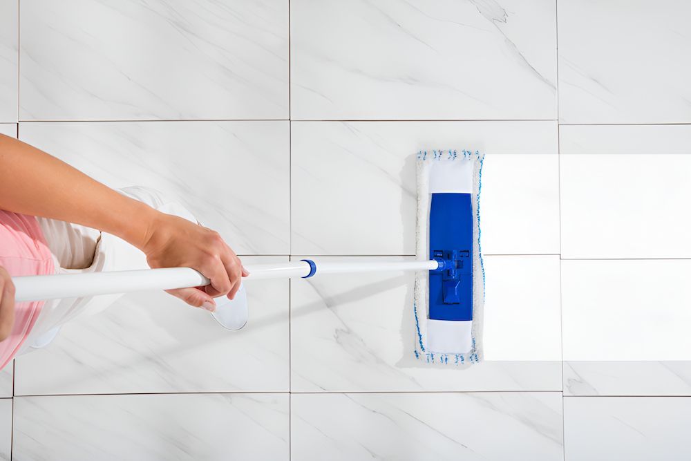 A Woman Is Cleaning A Tiled Floor With A Mop — Kyall Chalker Floor Sanding & Polishing In Macquarie, NSW
