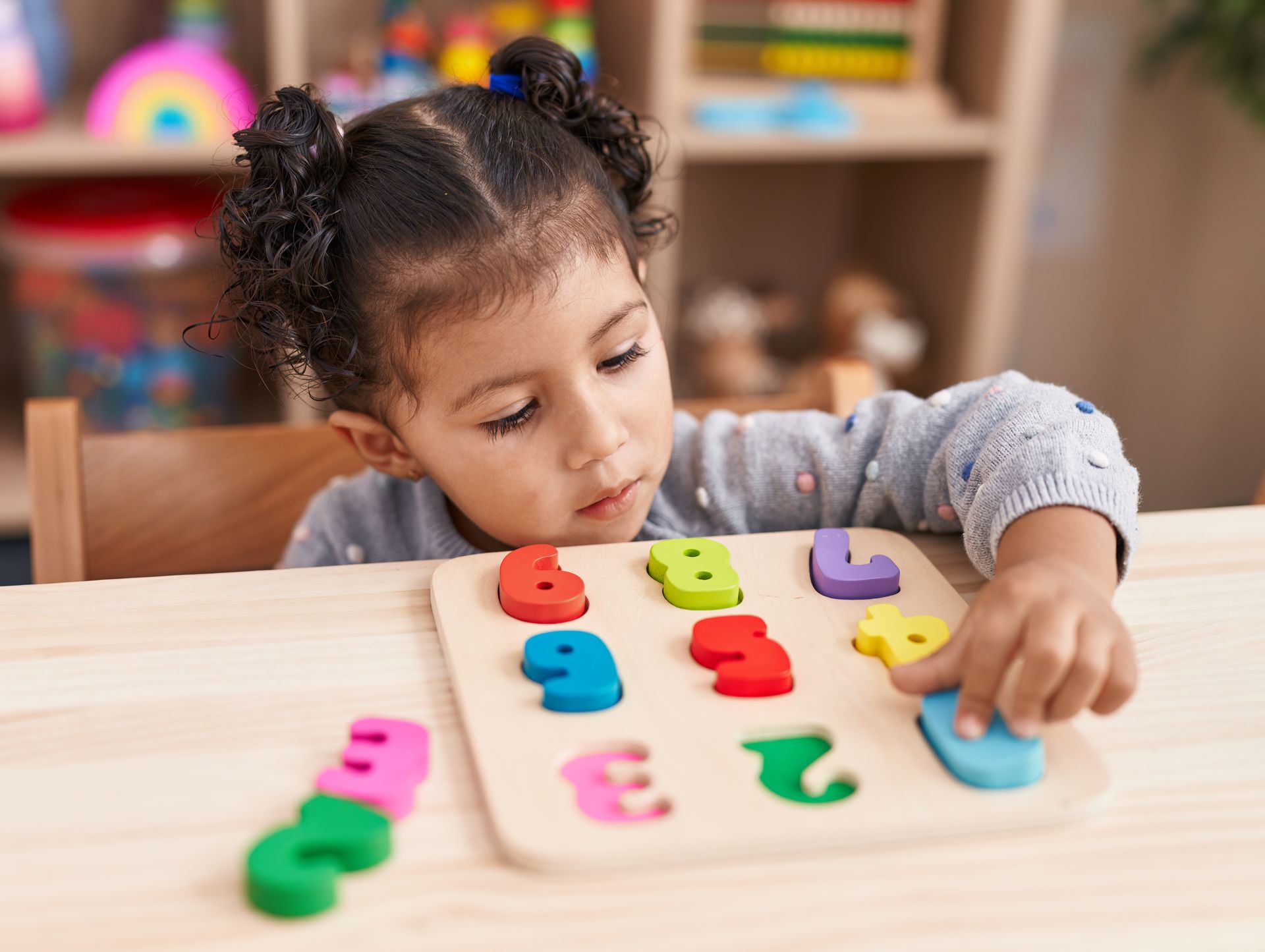 Child playing with colorful number blocks at a table, reaching for a blue block.