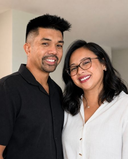 Smiling couple posing indoors, both in dark and white tops, standing close together.