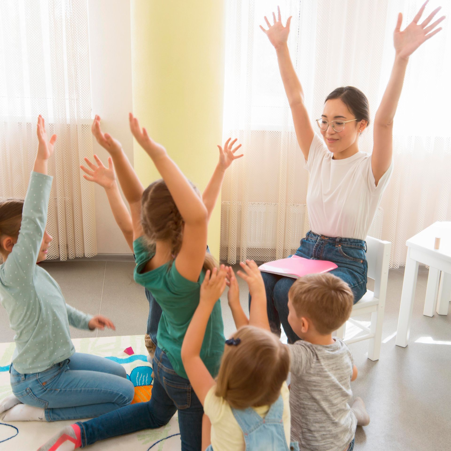 Children and teacher raising hands in a bright classroom during a group activity