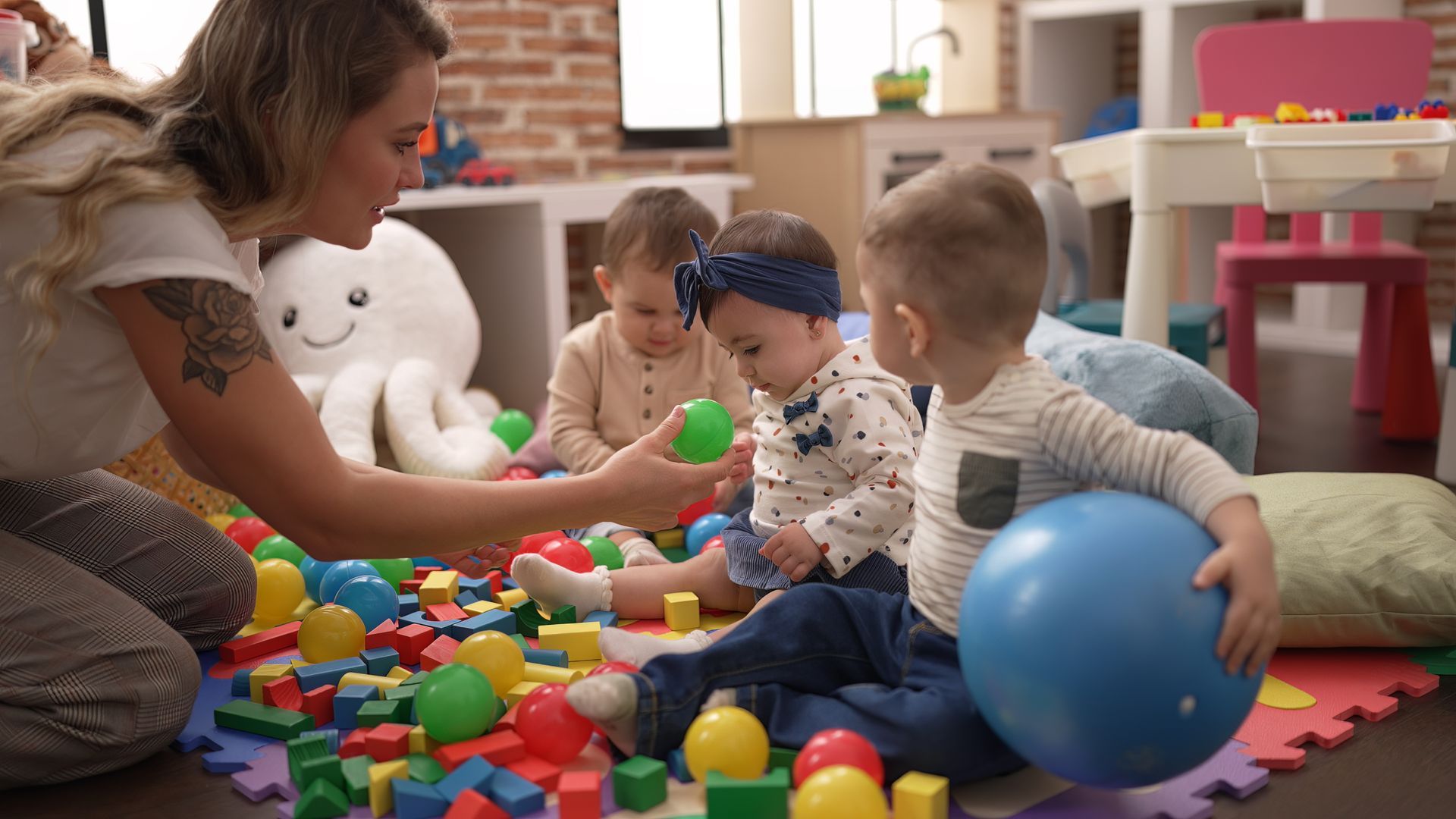 Children playing with colorful blocks and a blue ball on a foam mat while an adult watches nearby