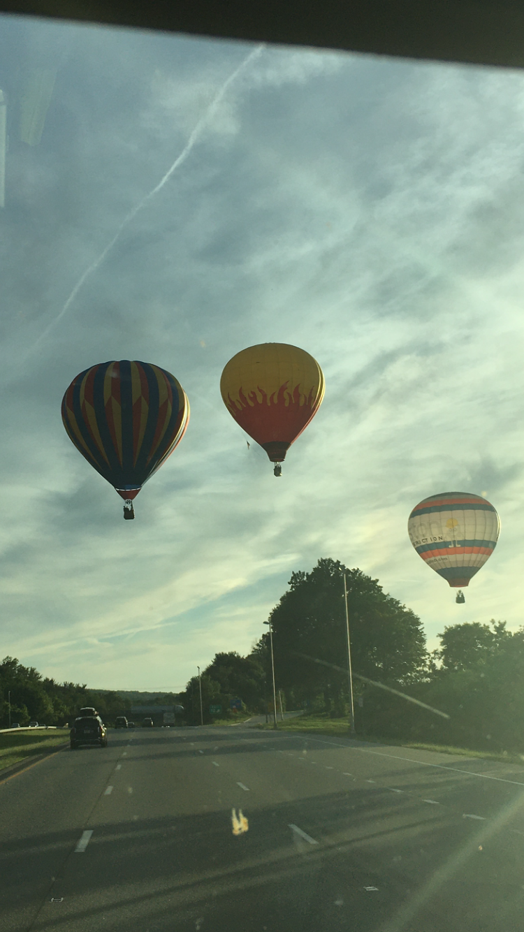 A group of hot air balloons are flying over a road.