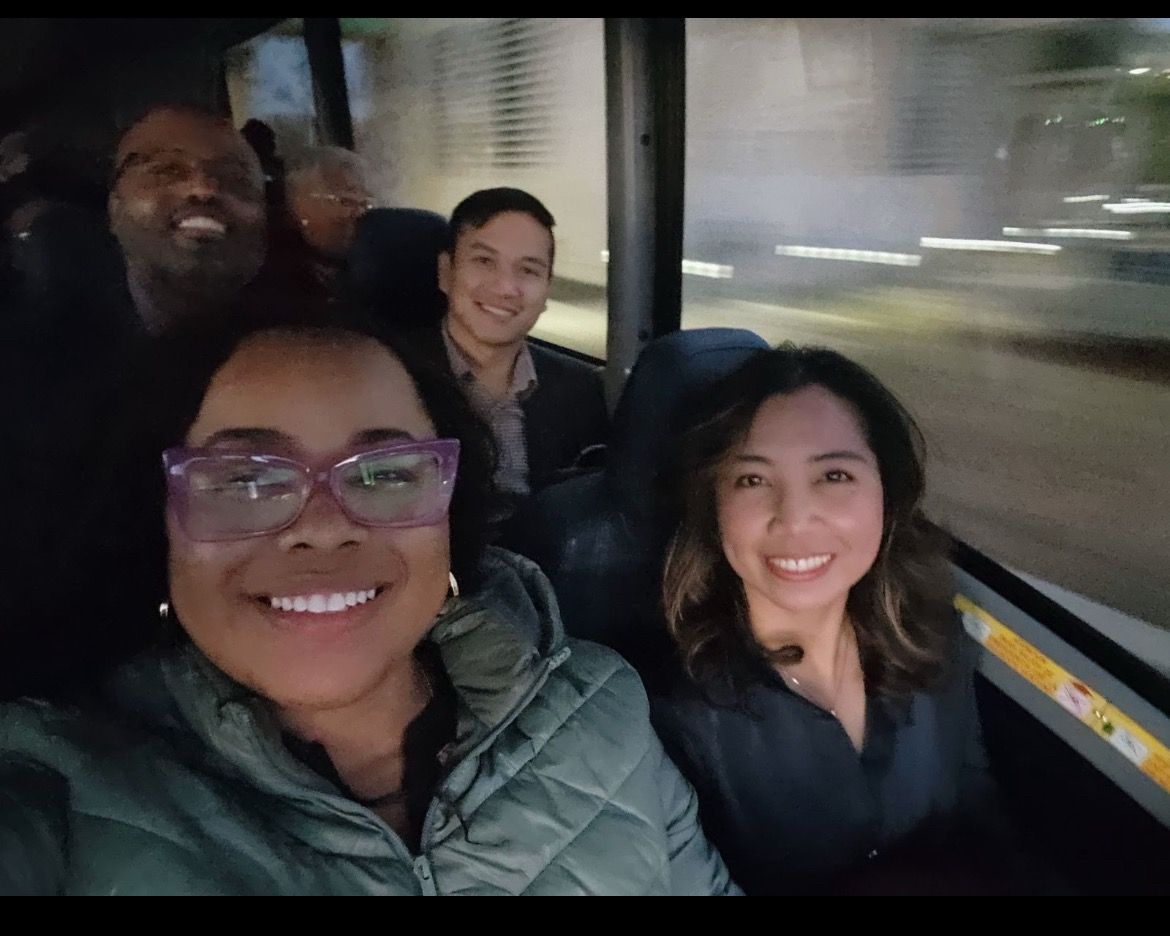 Four friends smiling inside a moving bus at night, with city lights streaking by the window.