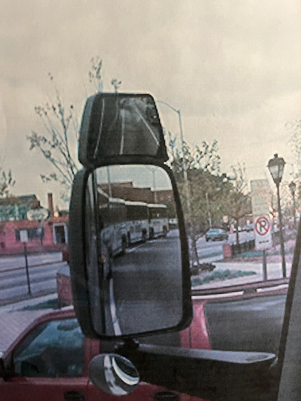 Close-up of a truck's side mirror reflecting a street and parked vehicles at dusk.