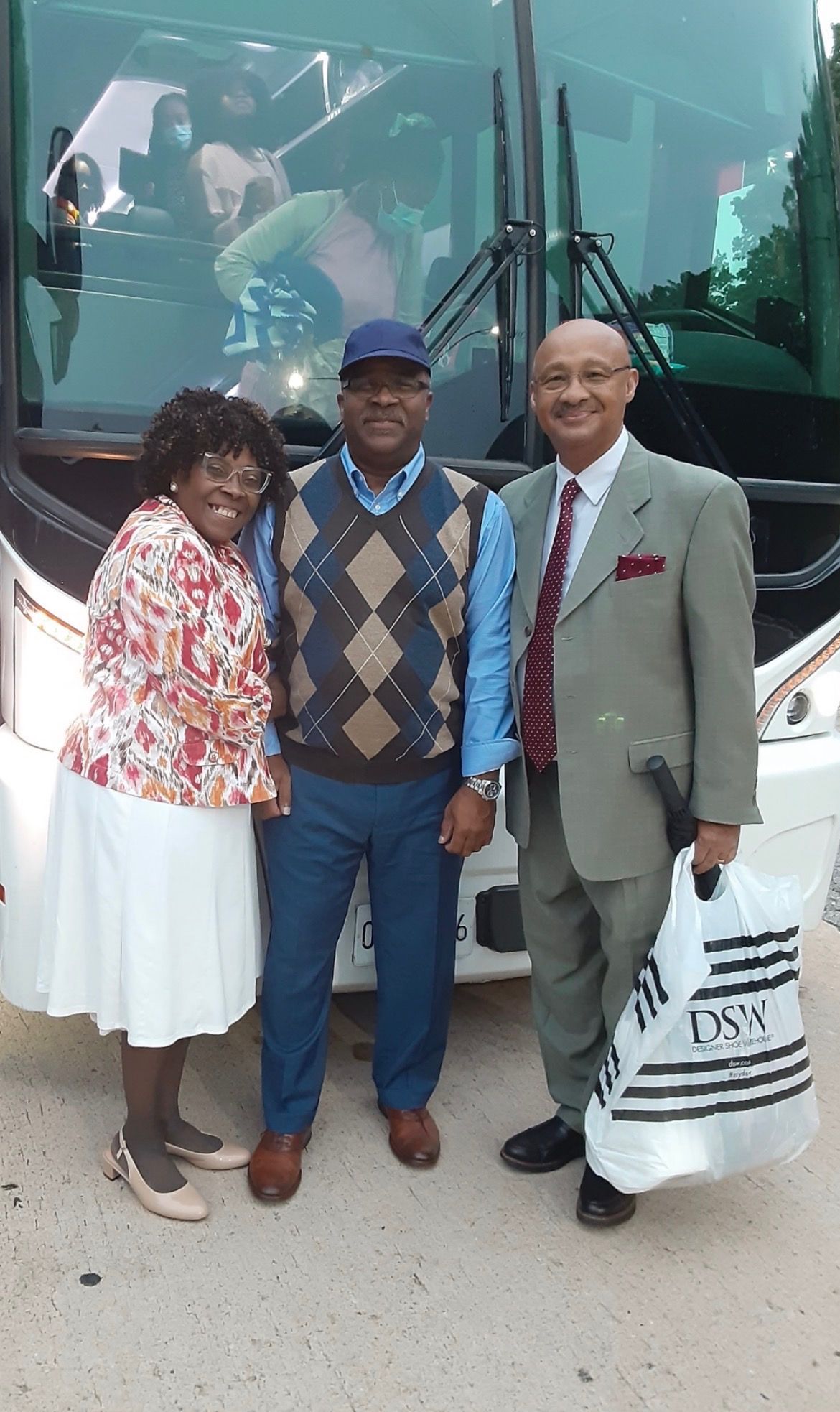 Three people posing in front of a large bus, smiling and standing close together.