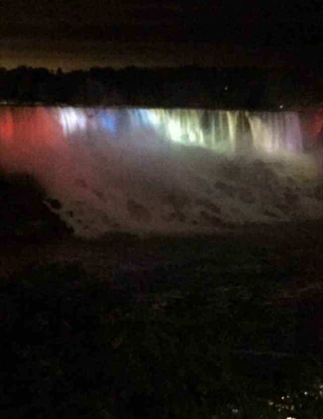 Nighttime view of a waterfall lit with red, white, and green lights beneath a dark sky