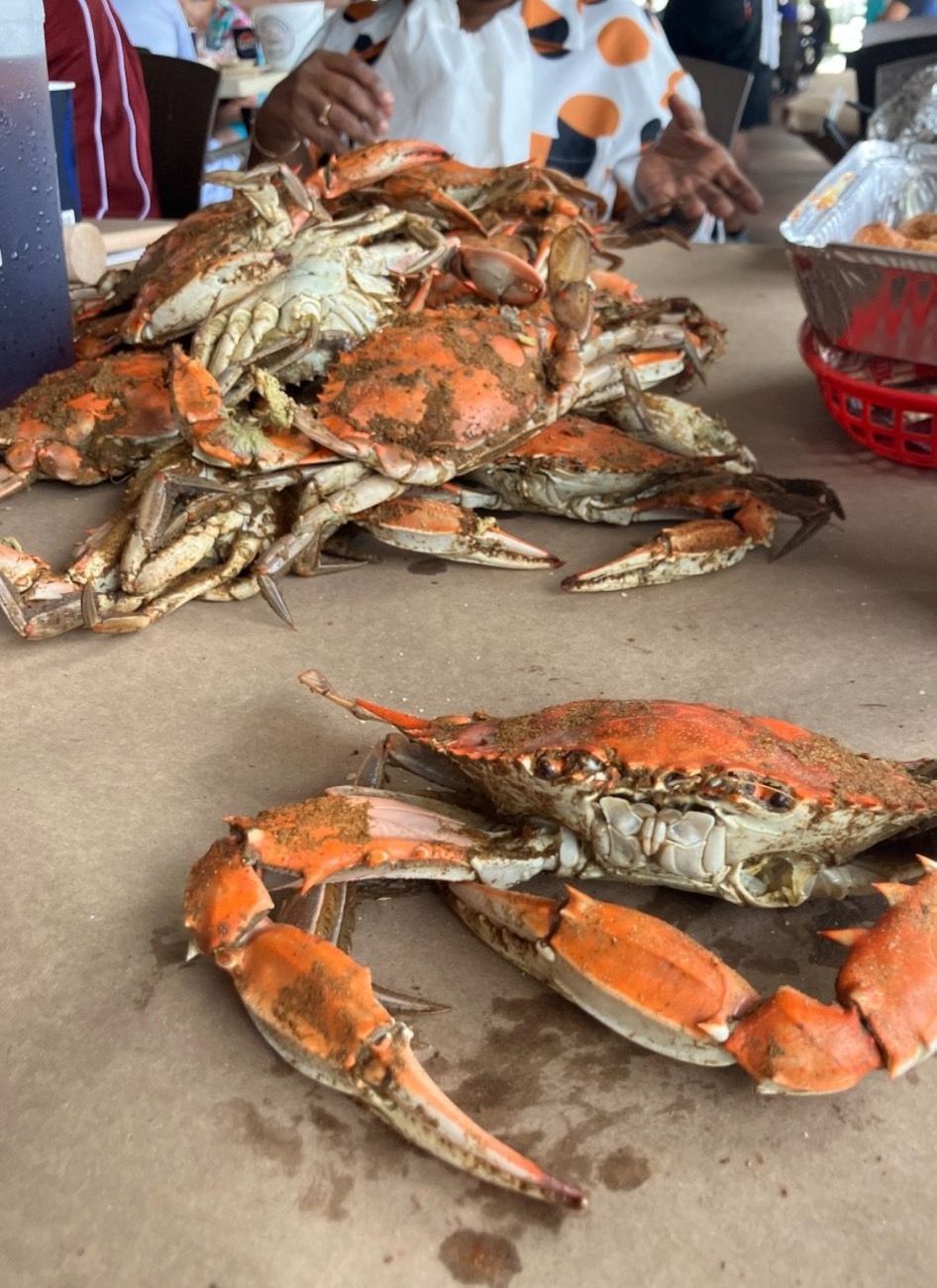 Fresh crabs piled on a table at a seafood market, with a person seated behind them.