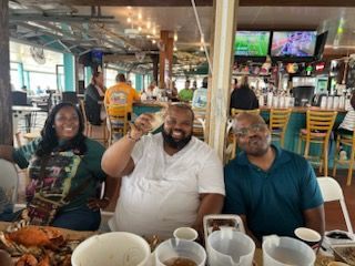 Three people smiling at a restaurant table with seafood and drinks, one raising a glass