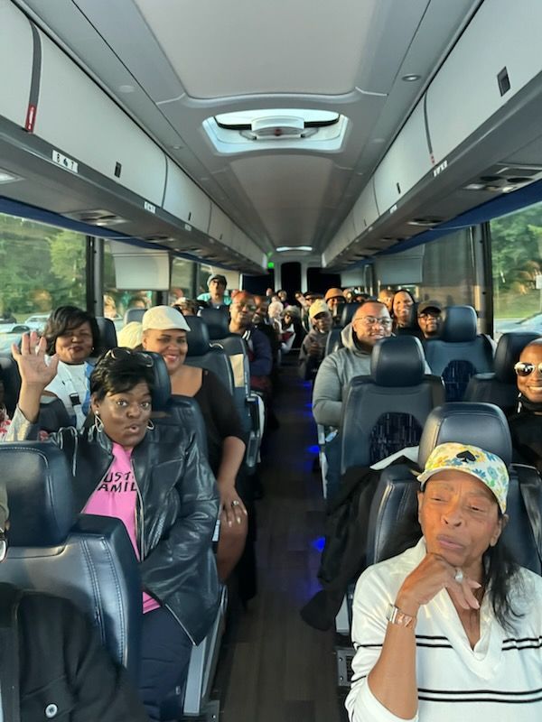 Passengers seated inside a bus, with several people waving and smiling.