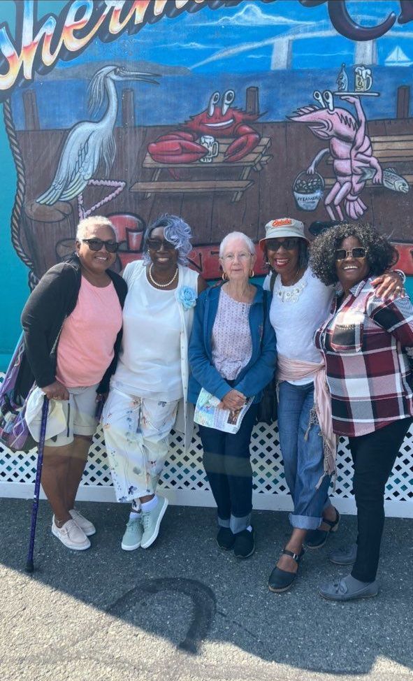 Five people posing together in front of a colorful mural on a sunny street.