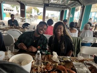 Two people smiling at a restaurant table with plates of food and drinks