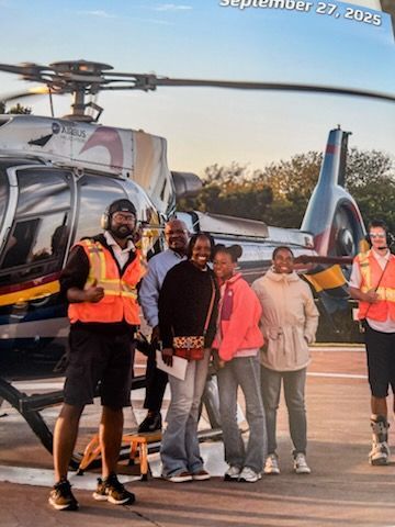 People standing beside a helicopter on a runway, some wearing orange safety vests