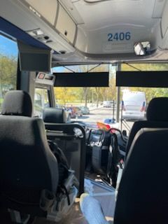 Inside a bus cabin with seats, handrails, and a view through the front windshield