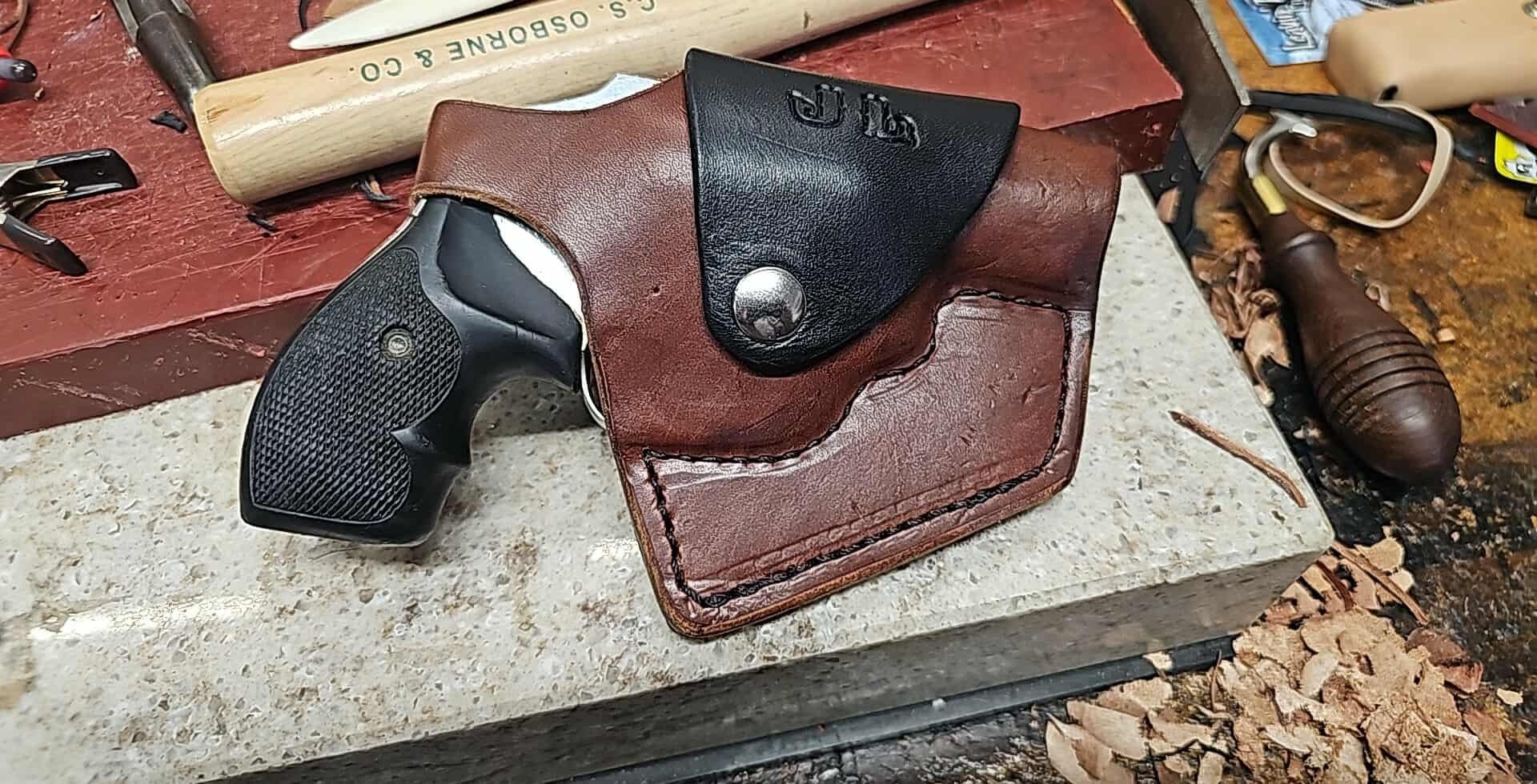 Leather holster with two black revolvers on a workbench, surrounded by tools and wood shavings