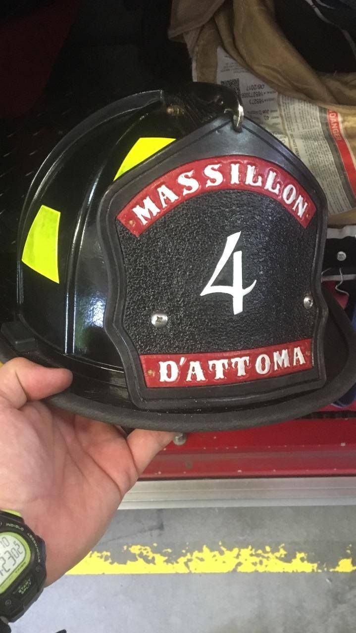 Black firefighter helmet labeled “Massillon D’Attoma” with number 4, held in a hand