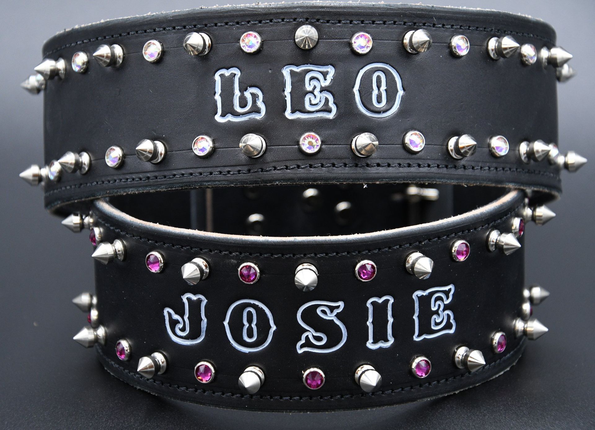 Black studded dog collars with white lettering, reading “LEO” and “JOSIE,” on a dark background