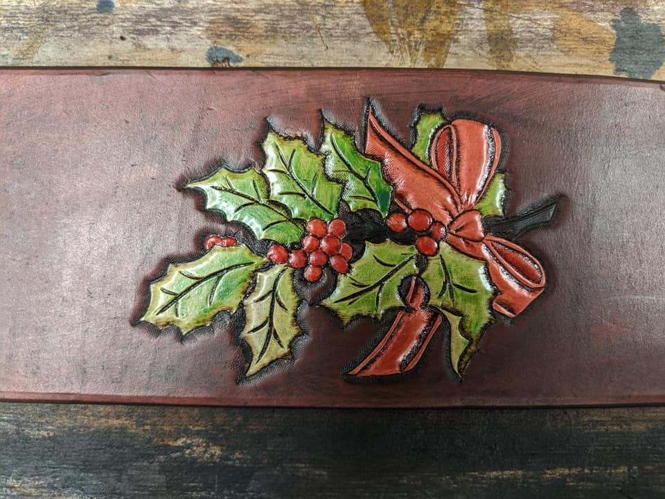 Holiday floral ornament with holly leaves, red berries, and a red bow on a wooden plaque