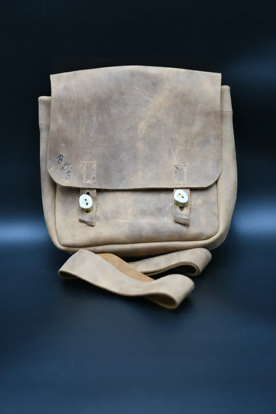 Beige canvas satchel bag with flap and strap on a dark background