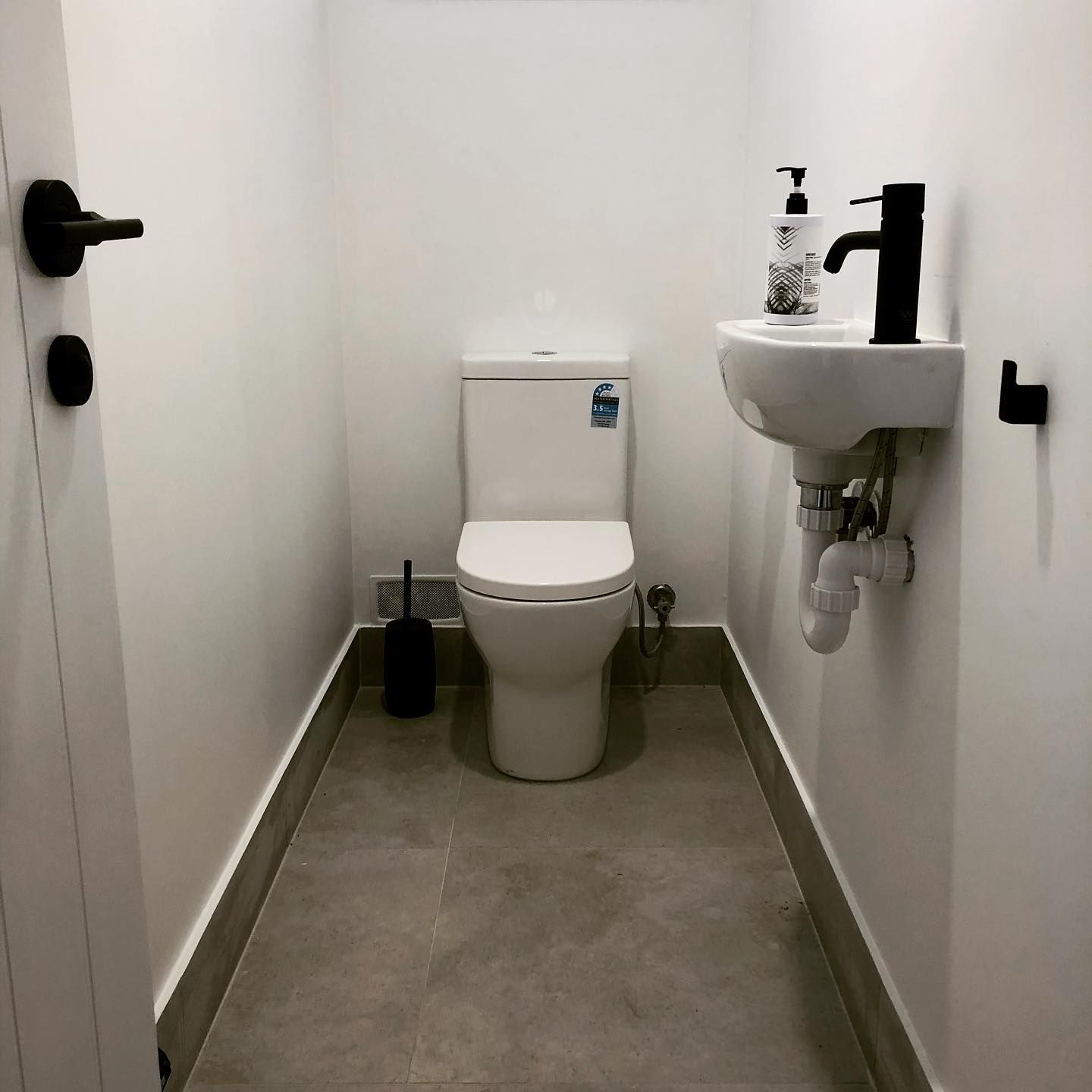 Small modern bathroom with a white toilet, sink, black fixtures, and gray tiled floor.