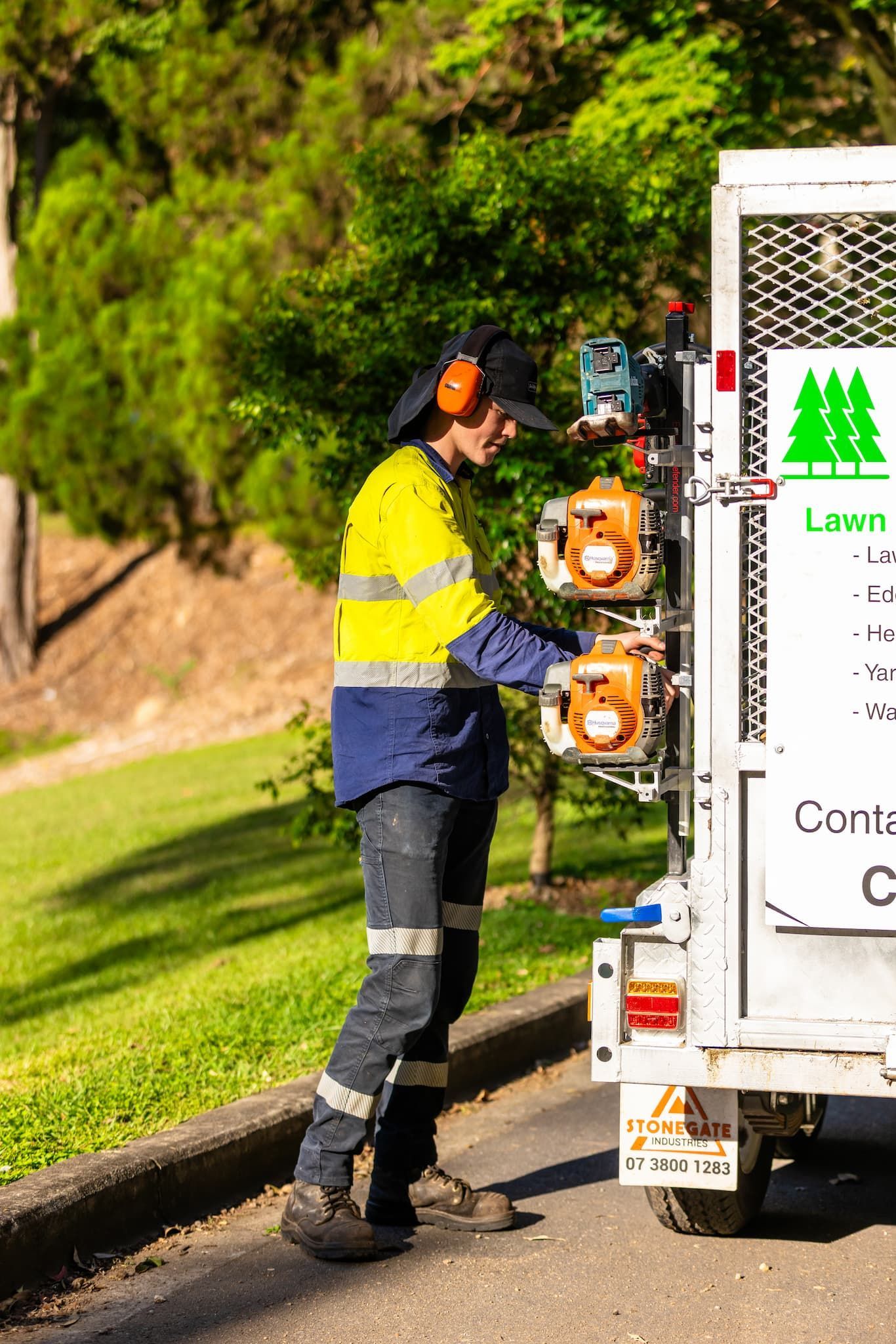 Person in high-vis gear loading chainsaws onto a trailer. Green trees in the background.