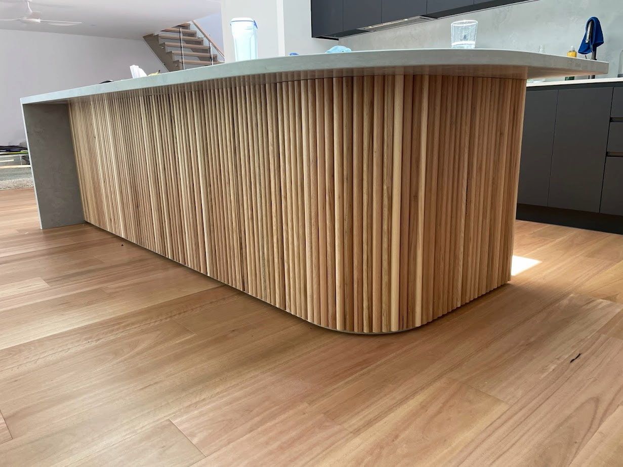 Modern kitchen island with curved wood paneling and a white countertop on a light wood floor