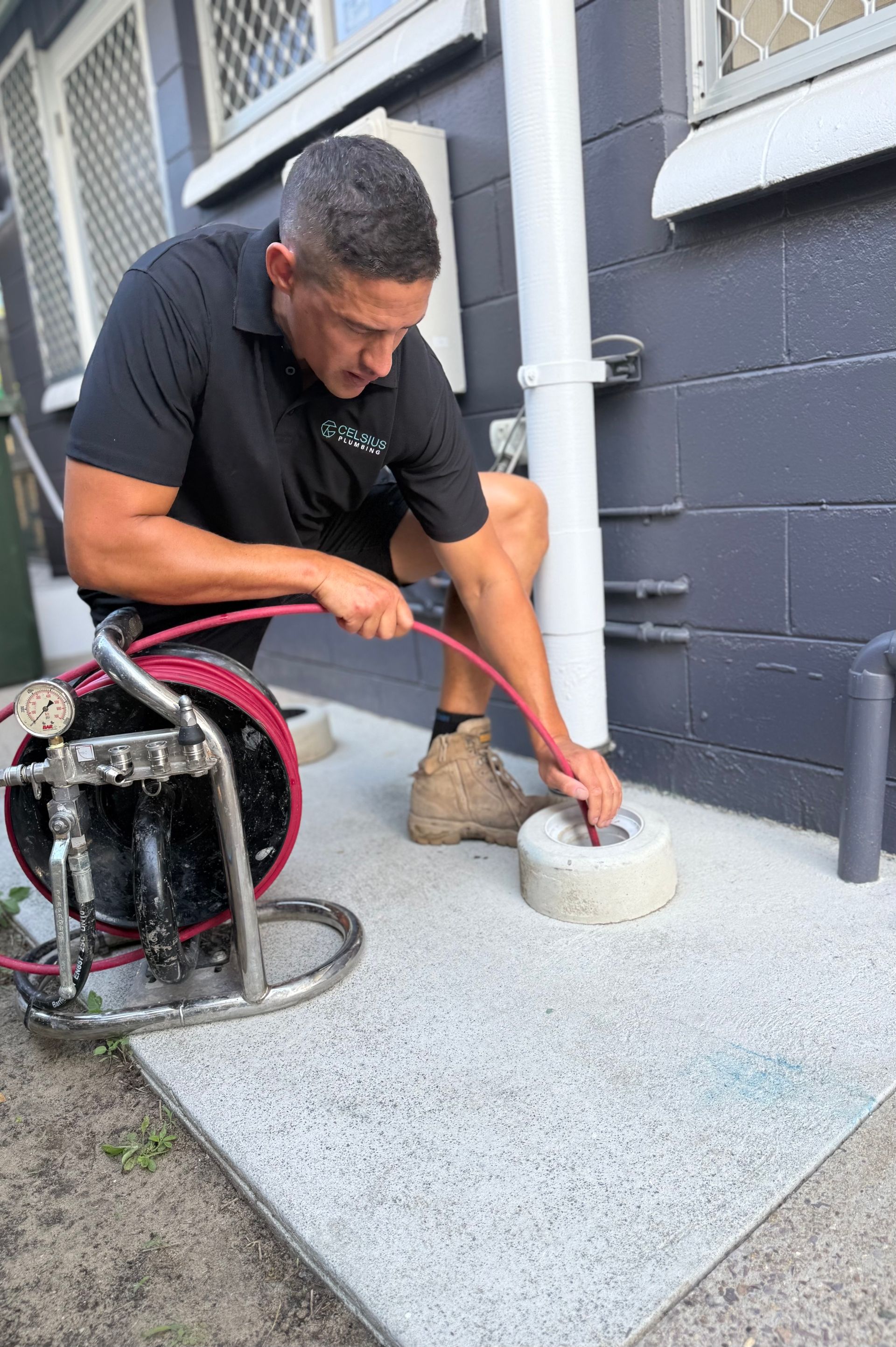 Man using plumbing equipment, inserting a hose into a drain on a concrete patio, outdoors.