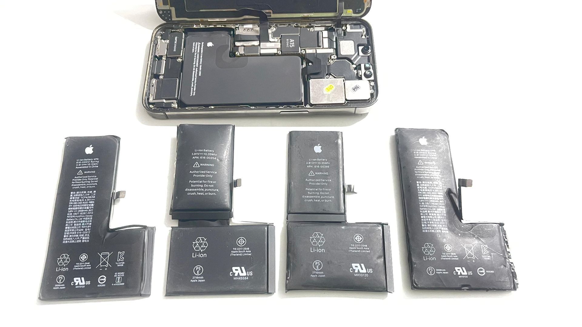 Un montón de baterías de iPhone están sentadas junto a otras, con un iPhone abierto encima de ellas.