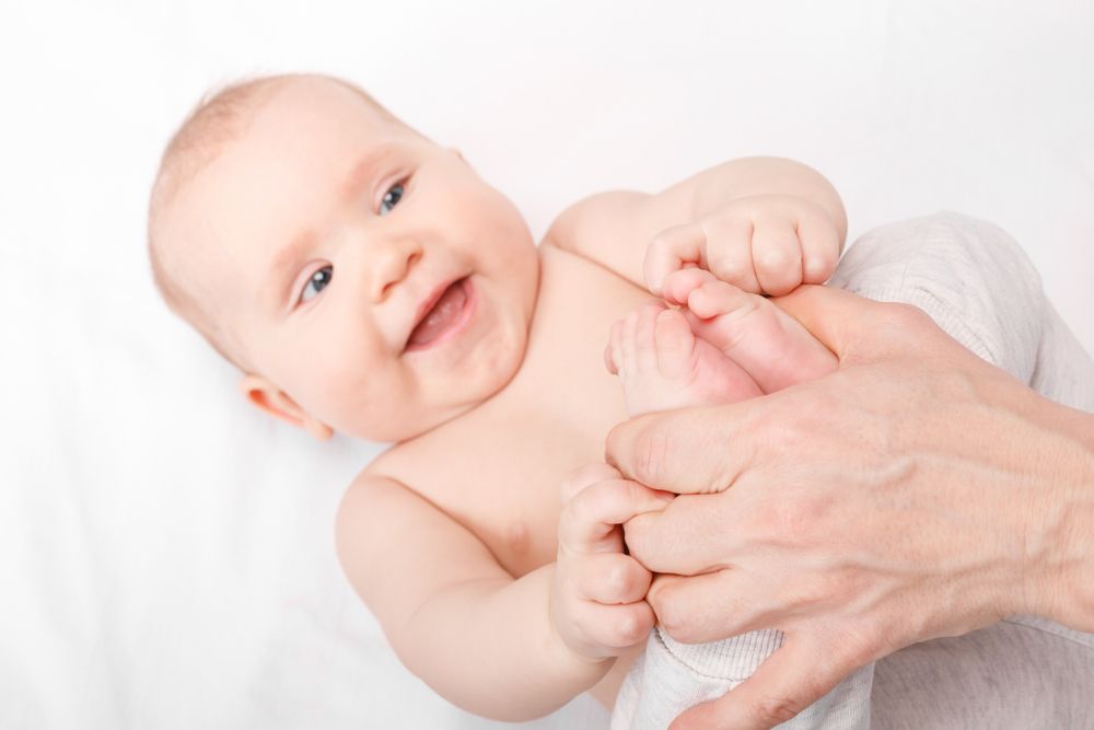 Un bébé est massé par une personne sur un lit.