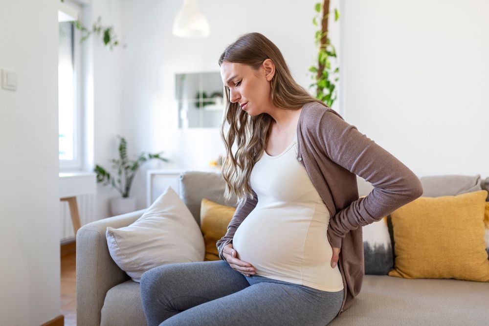 Une femme enceinte est assise sur un canapé et la retient de douleur.