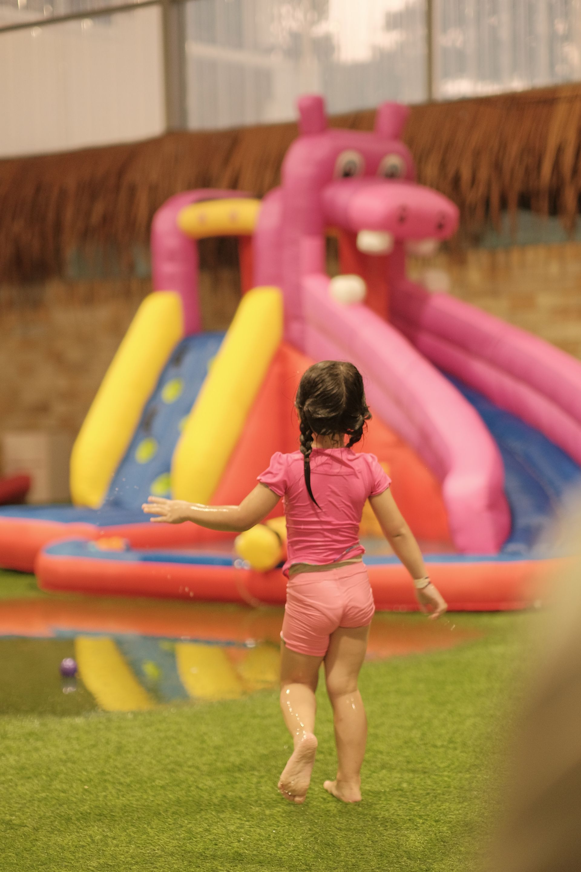 A little girl is running towards a pink inflatable hippo water slide.