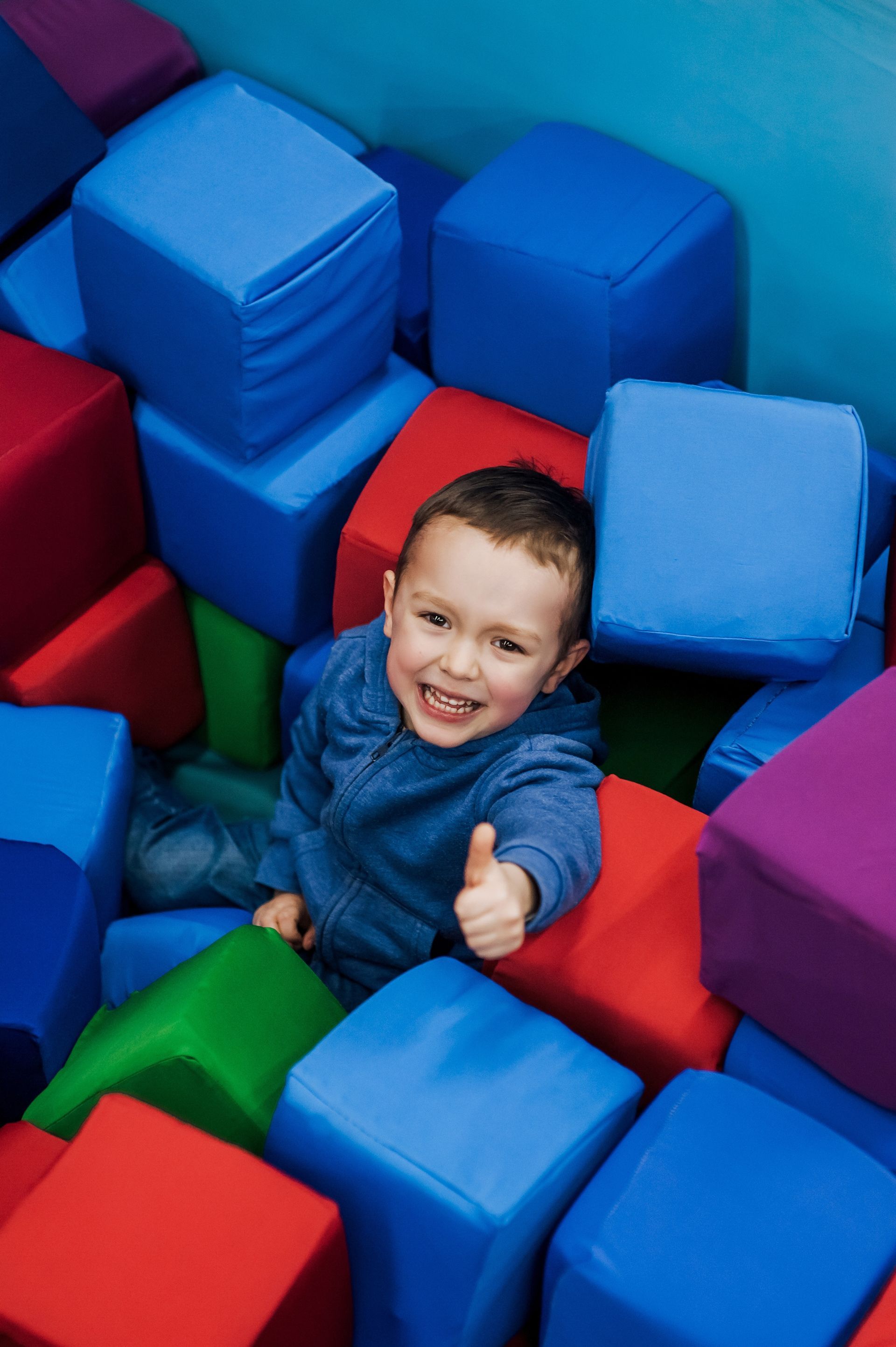 A young boy is laying in a pile of soft blocks and giving a thumbs up A young boy is laying in a pile of soft blocks and giving a thumbs up