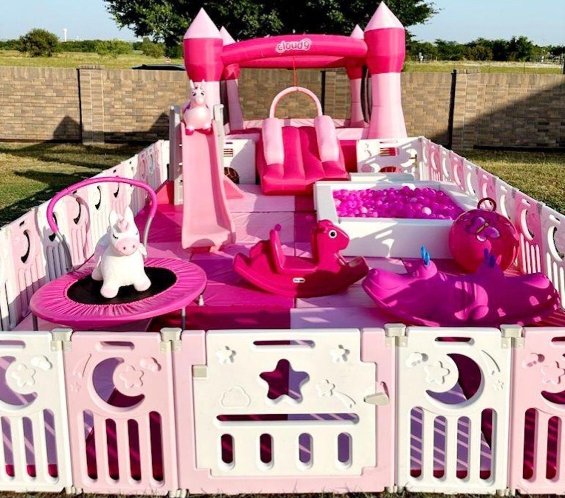 A pink playground with a castle , slide , trampoline , and unicorns.