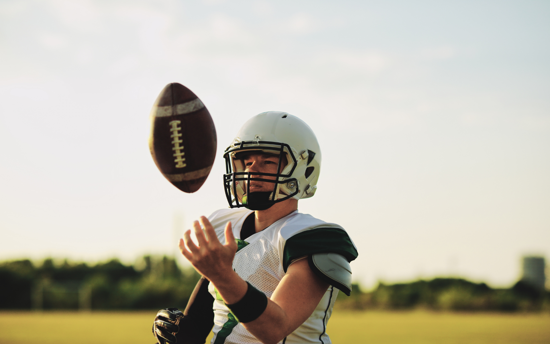 Football player, white helmet and uniform, tossing football in the air on field.