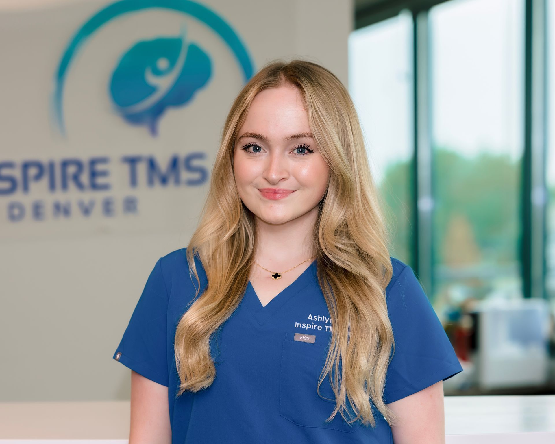 Woman in blue scrubs standing in front of an Inspire TMS Denver sign.