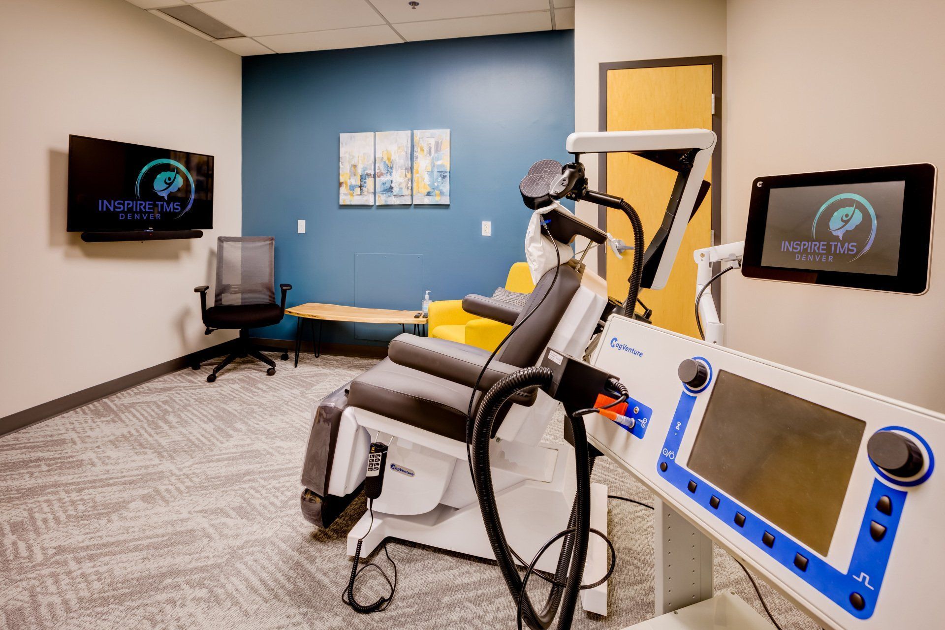 Modern clinical exam room with a reclining treatment chair, monitors, and blue-gray walls