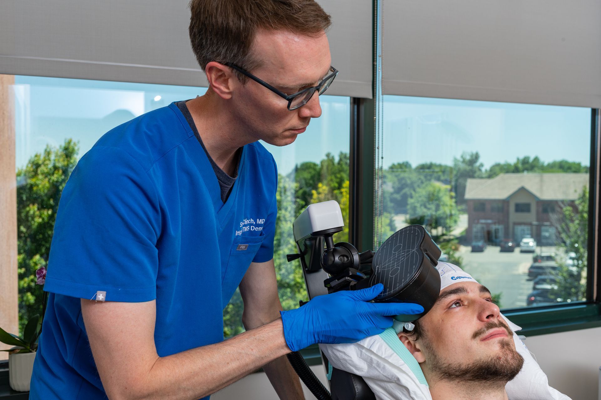 Healthcare worker in blue scrubs examining a patient's eye with a handheld device in a clinic.