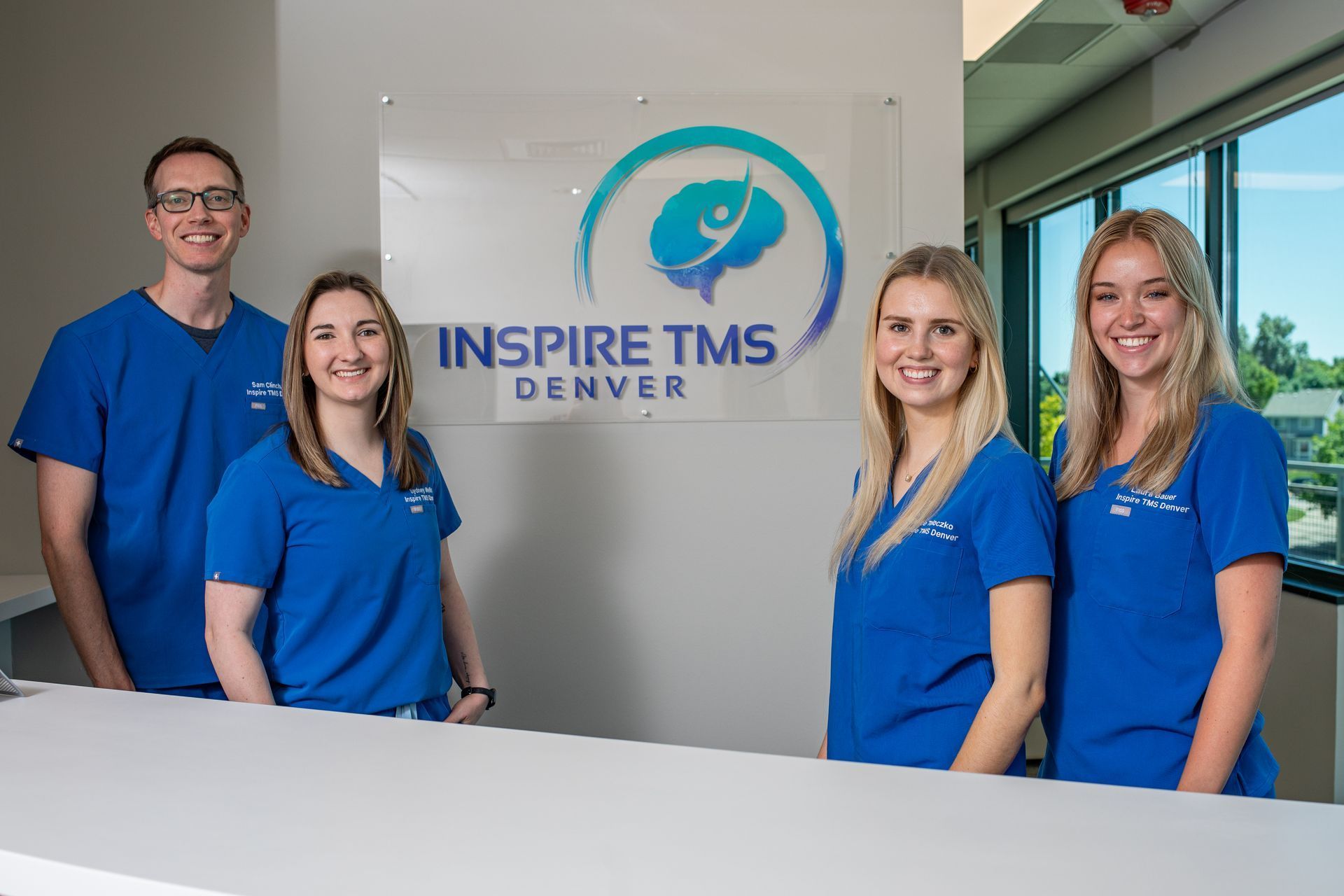 Four staff in blue scrubs stand at an Inspire TMS Denver reception desk.