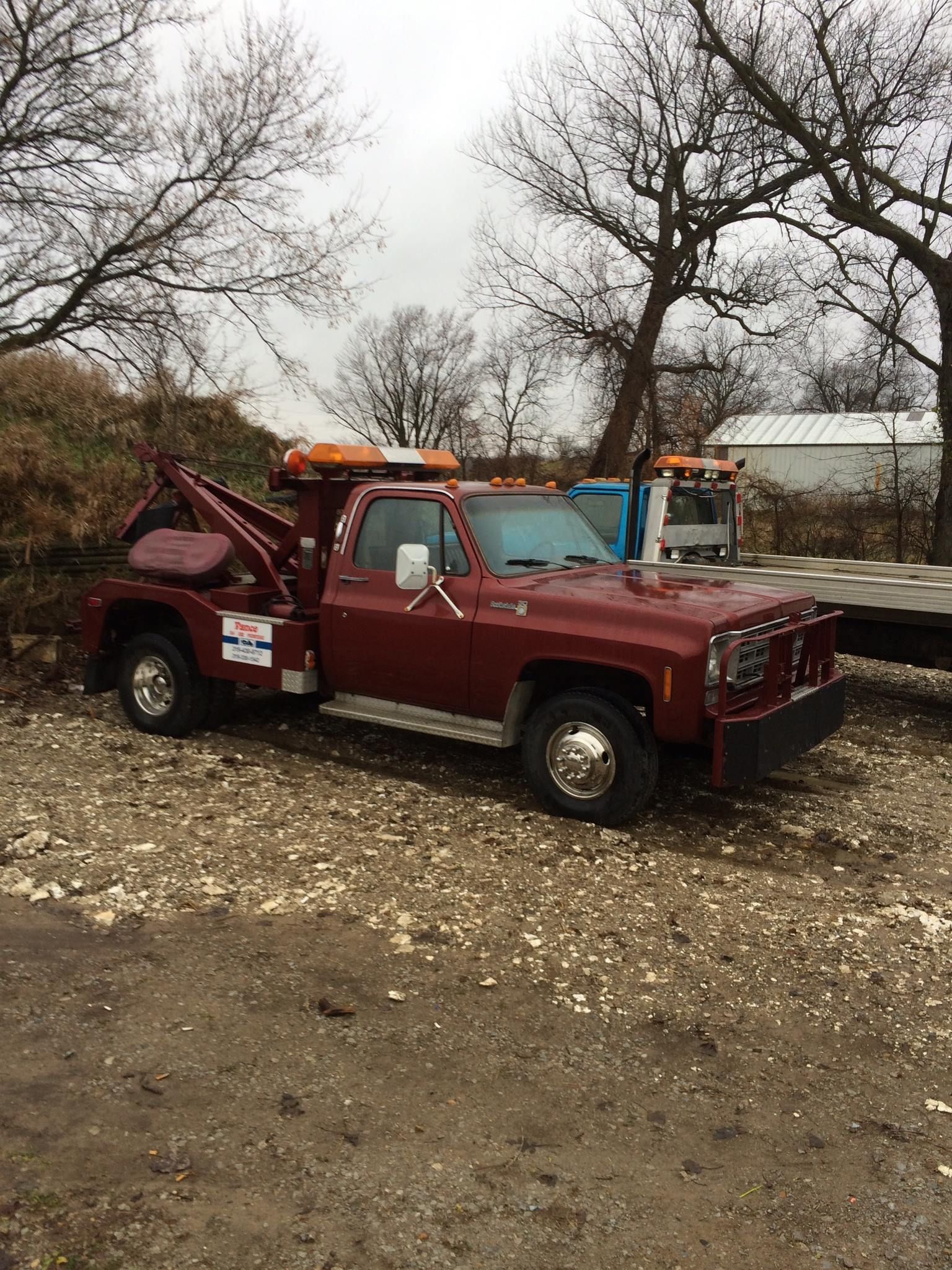 Red tow truck parked on gravel, trees in background, overcast day.
