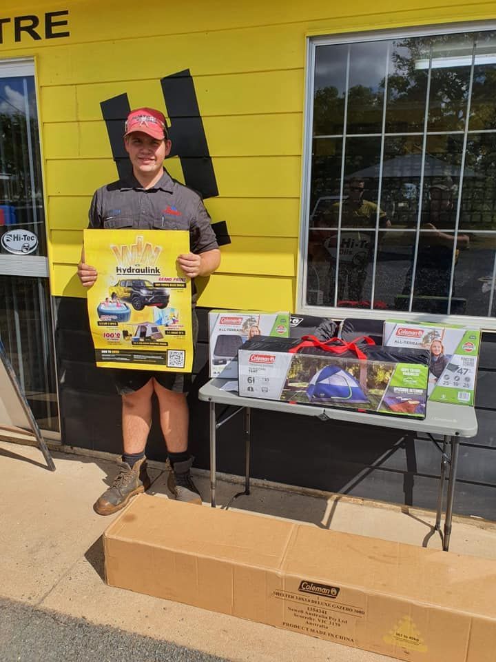 Person standing outside a yellow storefront holding a poster beside a display table and cardboard box.